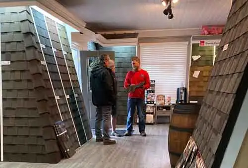 Two professionals engage in a consultation surrounded by Owens Corning shingles in a well-organized showroom